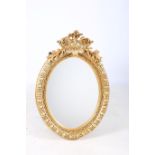 A CONTINENTAL GILT FRAMED MIRROR the oval bevelled glass plate within a C scroll flower head and