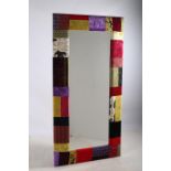 A BEVELLED GLASS MIRROR the shaped plate within a patchwork upholstered frame 201cm x 101cm