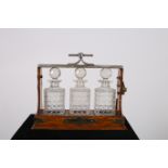 A 19TH CENTURY OAK AND PLATED TANTALUS containing three cut glass decanters with stoppers stamped