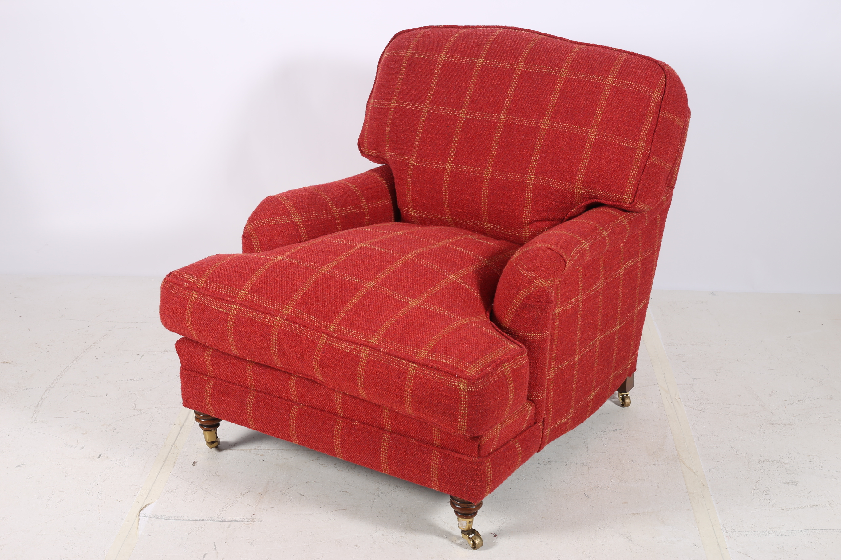 AN UPHOLSTERED EASY CHAIR with loose cushions and shaped arms on turned legs with brass caps and