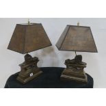 A PAIR OF COMPOSITION BRONZED TABLE LAMPS each of architectural form surmounted by a lion shown