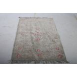 AN ORIENTAL WOOL RUG the beige ground with central stylized foliate panel within a conforming