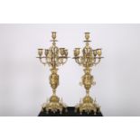 A PAIR OF HEAVY BRASS FIVE BRANCH CANDELABRA each with an urn column with scroll decoration above a