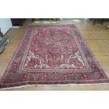 A HERIZ WOOL RUG the wine ground with central panel filled with flower heads and foliage within a