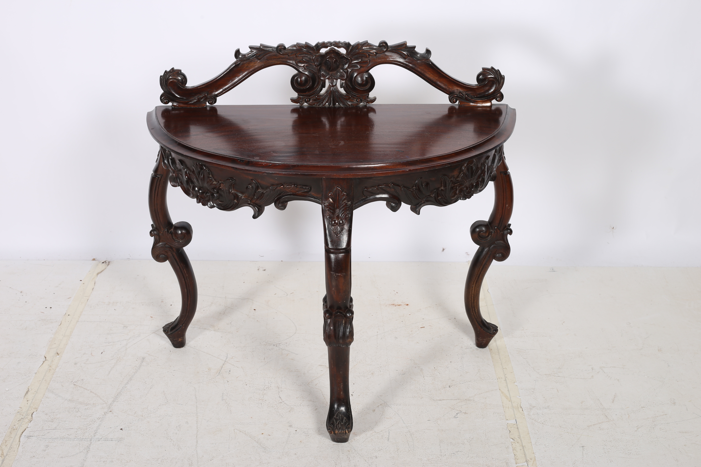 A MAHOGANY SIDE TABLE of demilune outline with carved back and frieze on cabriole legs with scroll