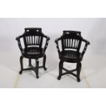 A PAIR OF EBONISED TUB SHAPED SWIVEL CHAIRS with scroll over back and pierced vertical splats with