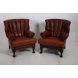 A PAIR OF BROWN HIDE UPHOLSTERED WING CHAIRS each with scroll over arms and loose cushions on