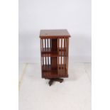 AN EDWARDIAN MAHOGANY REVOLVING BOOKCASE the square top above open compartments with slatted