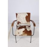 A RETRO HARDWOOD AND BLACK METAL ELBOW CHAIR with cowhide upholstered back and seat on cylindrical