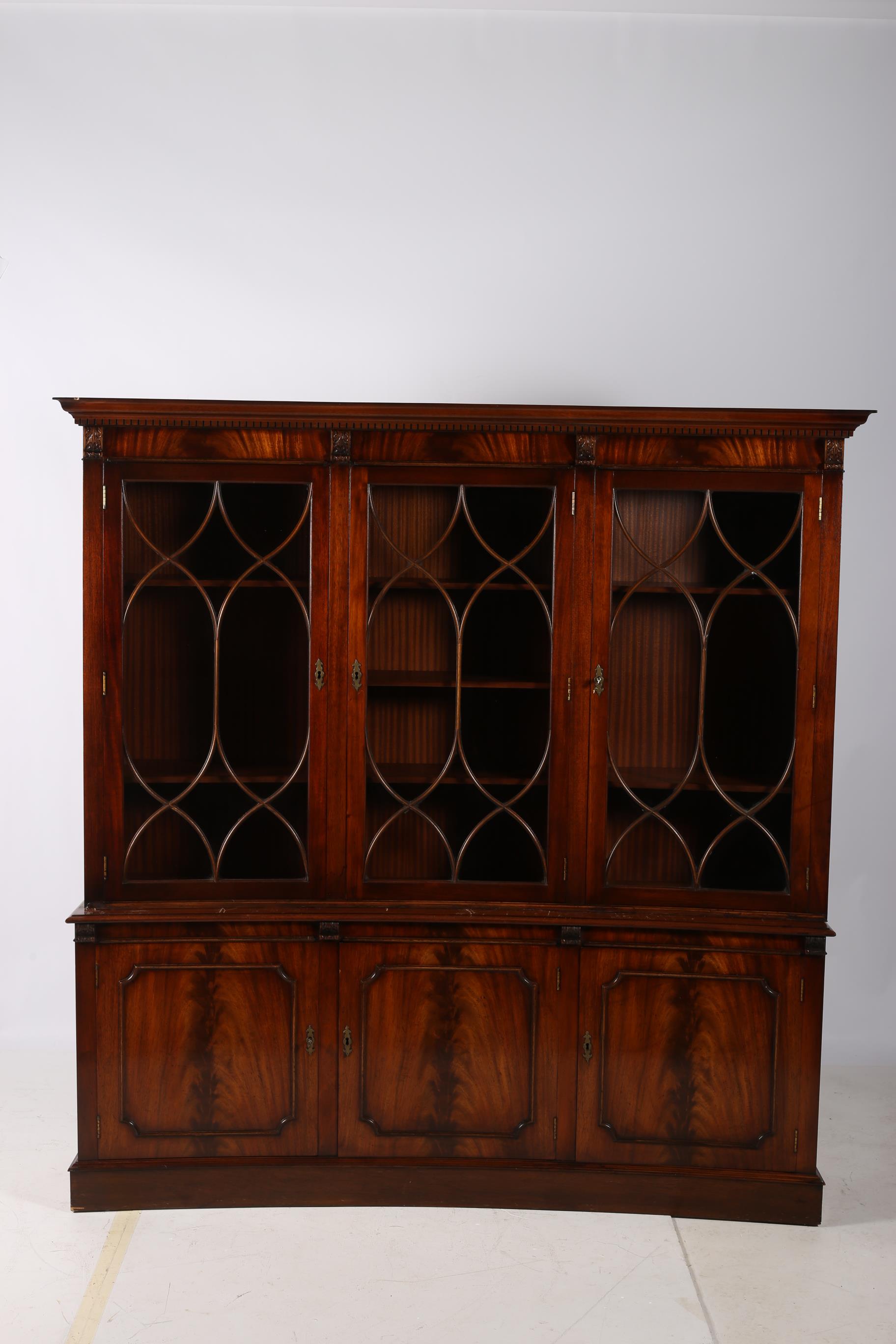 A GEORGIAN DESIGN MAHOGANY LIBRARY BOOKCASE of concave outline the dentil moulded cornice above