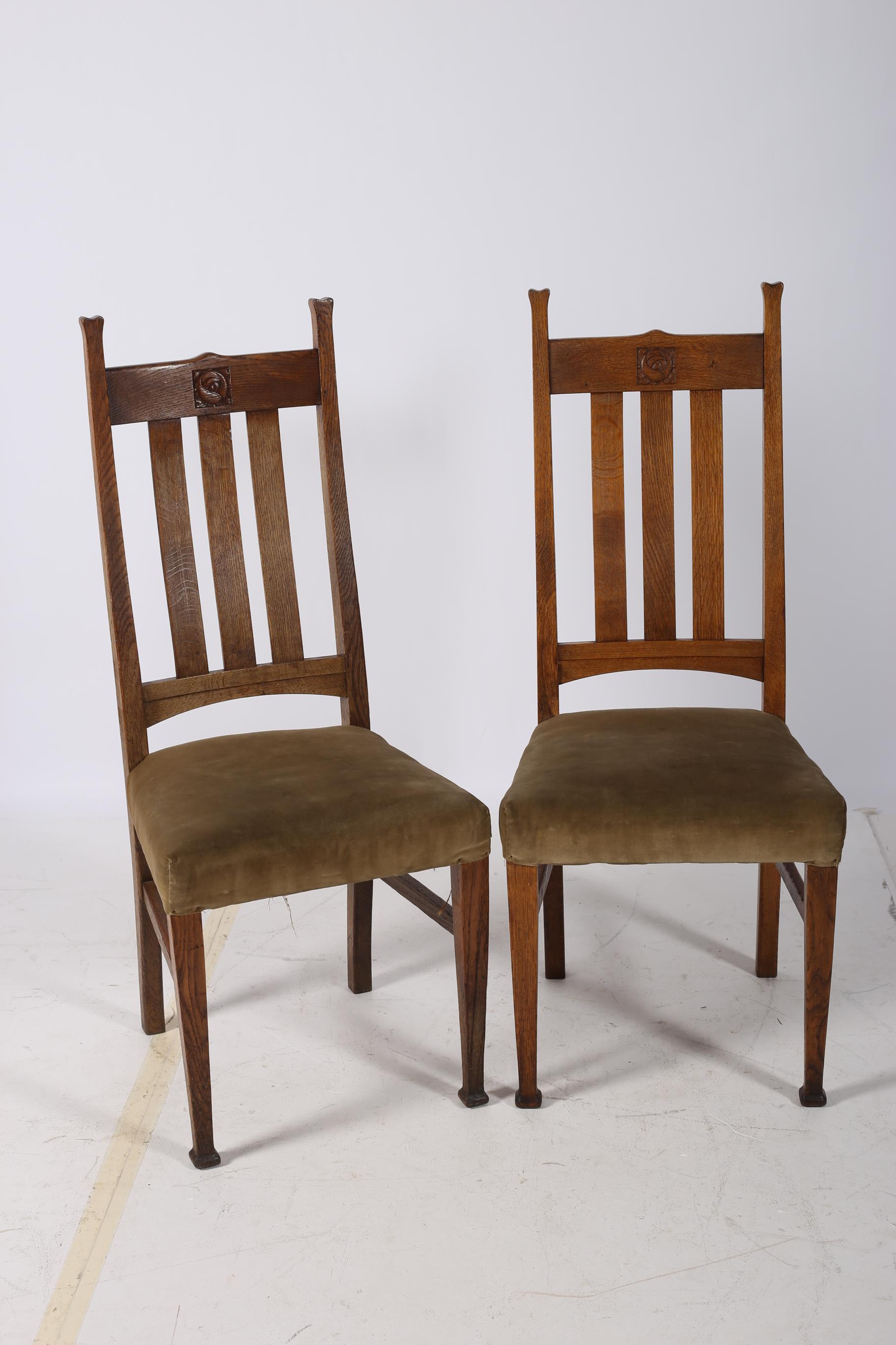 A PAIR OF ARTS AND CRAFTS OAK SIDE CHAIRS each with a shaped top rail and carved panel with