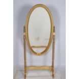 A CONTINENTAL GILTWOOD CHEVAL MIRROR the oval bevelled glass plate within a moulded frame raised on