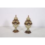 A PAIR OF CONTINENTAL GLAZED PORCELAIN LIDDED URNS the green and gilt ground decorated with pastrol