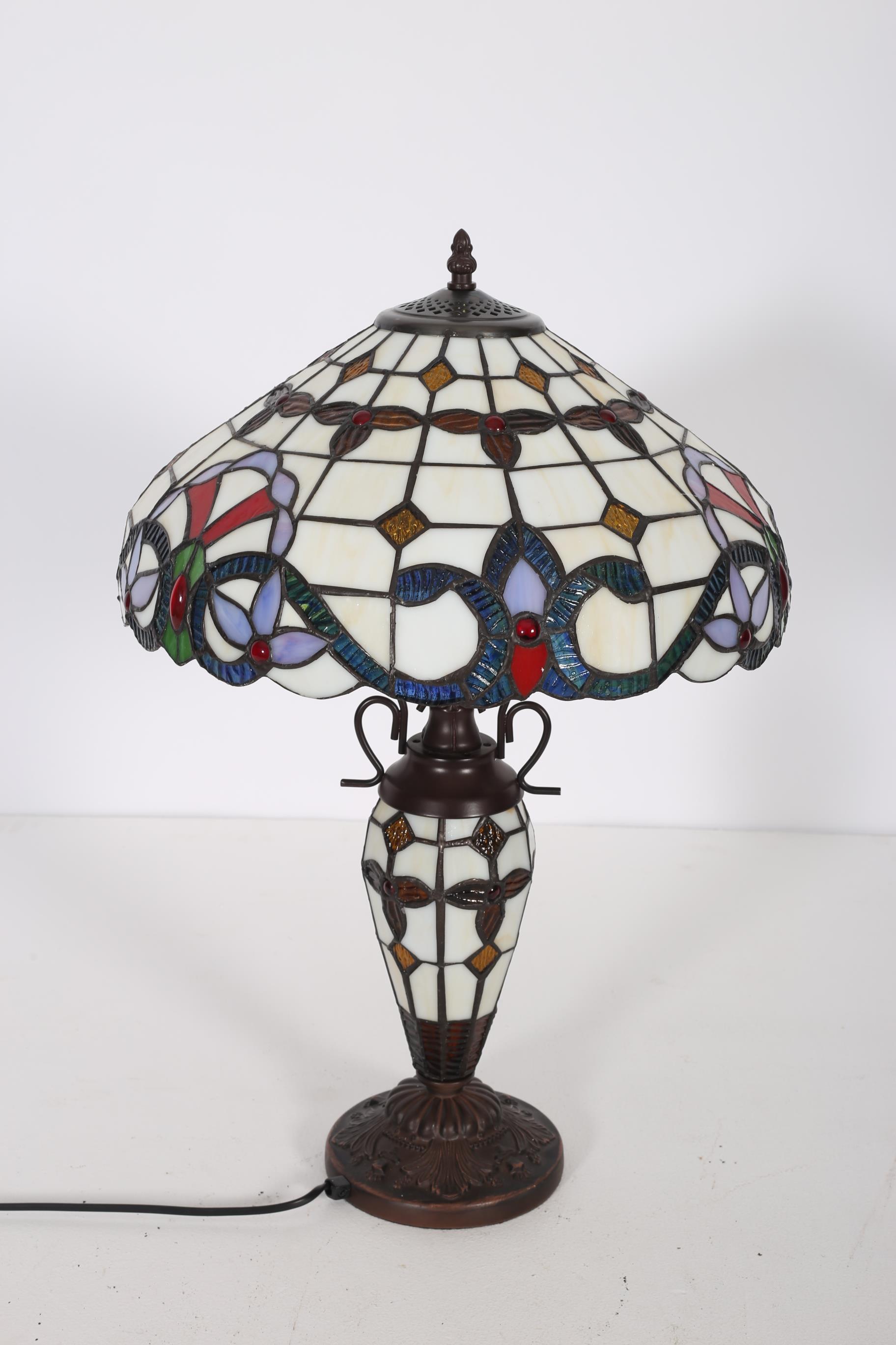 A TIFFANY DESIGN BRONZED TABLE LAMP the multicoloured shade above a baluster column on a circular