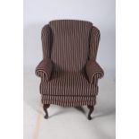 A QUEEN ANNE DESIGN MAHOGANY AND UPHOLSTERED WING CHAIR with scroll over arms and loose cushion on