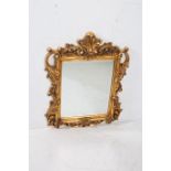 A CONTINENTAL GILT FRAMED MIRROR the rectangular bevelled glass plate within a foliate flowerhead