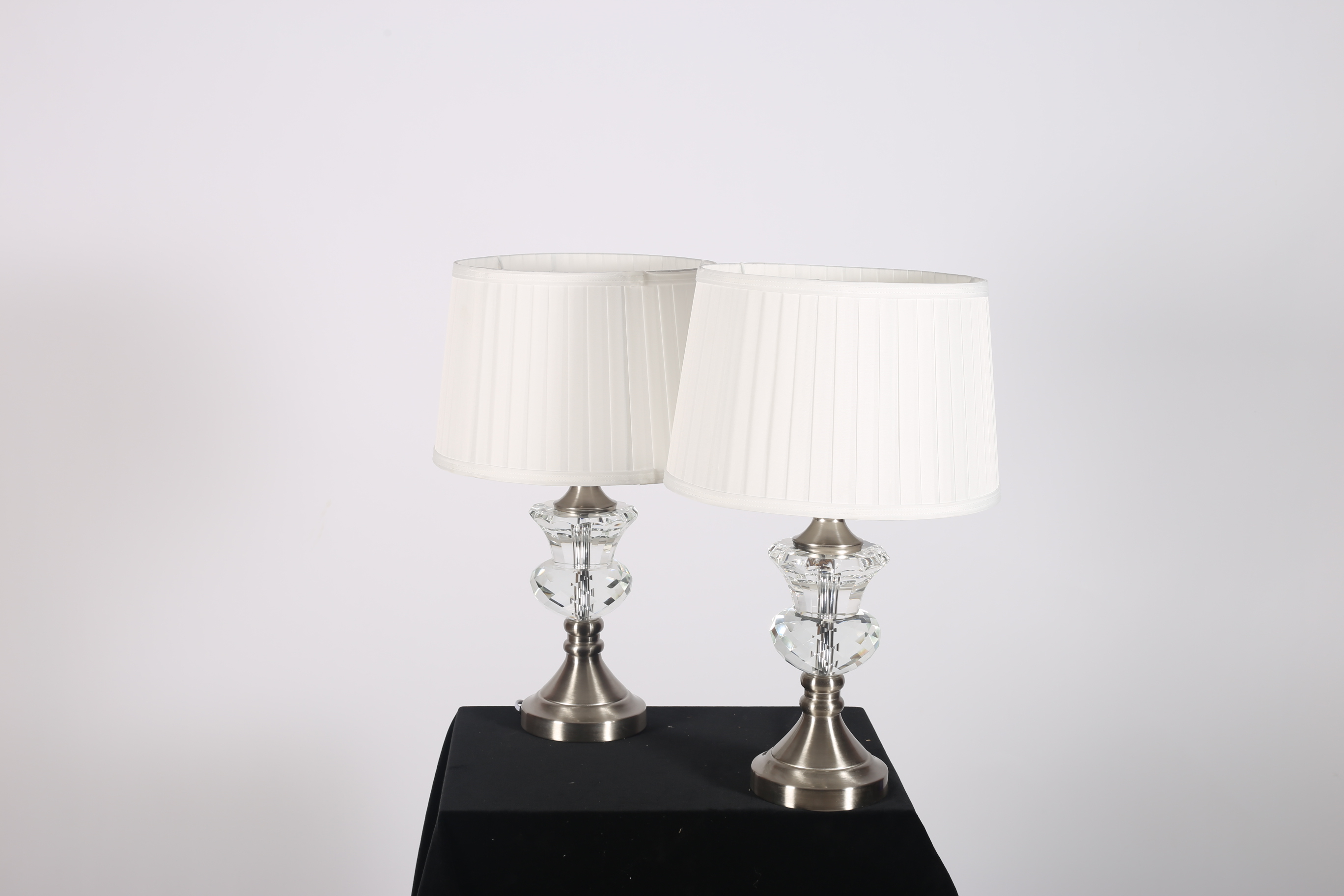 A PAIR OF WHITE METAL AND CUT GLASS TABLE LAMPS each with a faceted urn column above a circular