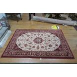 A WOOL RUG the light pink and wine ground with central floral panel within a conforming border