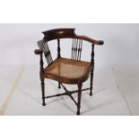 A MAHOGANY CORNER CHAIR the curved top rail with scroll arms and caned seat on turned legs