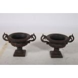 A PAIR OF CAST IRON GARDEN URNS each of semi lobed Campana form with scroll handles on square base