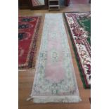 A CHINESE WOOL RUNNER the light pink ground with central floral panel within a conforming border