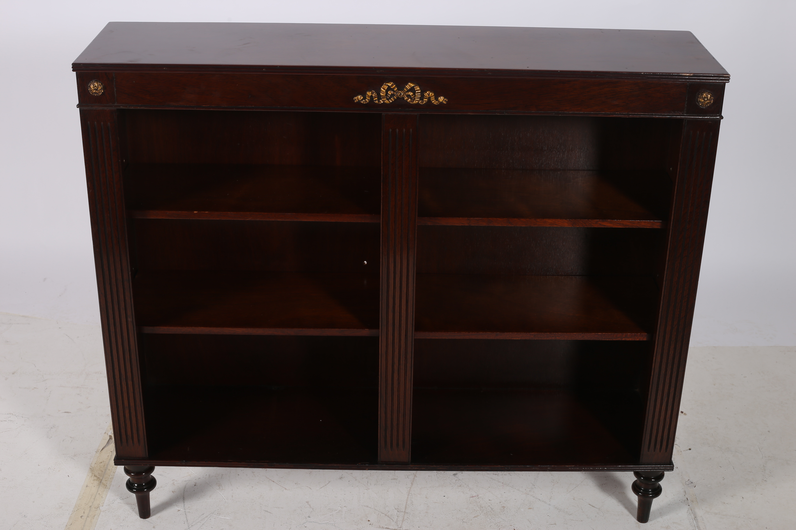 A REGENCY DESIGN MAHOGANY OPEN FRONT BOOKSHELF of rectangular outline the shaped top with a reeded