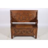 A CIRCA 1950s CARVED OAK MONKS BENCH the rectangular hinged top above a hinged seat with carved