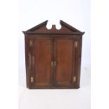 A GEORGE lll OAK HANGING CORNER CABINET the architectural pediment above a pair of panelled doors