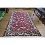 A PERSIAN HANDMADE WOOL RUG the wine ground with central panel filled with flowerheads serrated