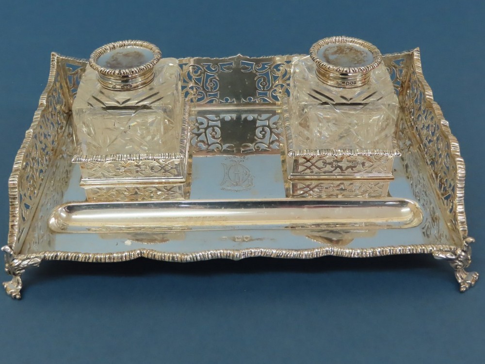 An Edwardian silver ink stand with pierced galleried sides, two cut glass ink bottles, pen well on