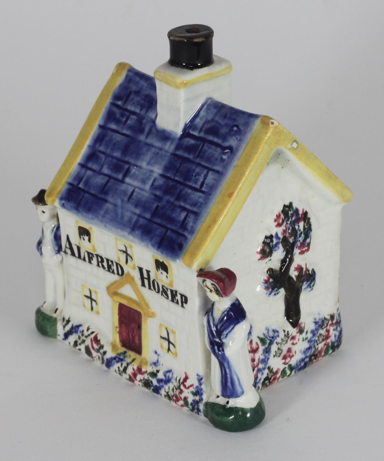 An early 19th century Staffordshire pottery money box shaped as a cottage, flanked by male and