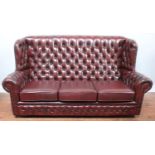 A Chesterfield style button upholstered, wingback three seat leather sofa in oxblood, with typical