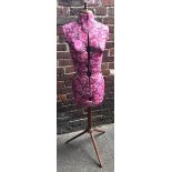 An adjustable dressmakers dummy, with a pink floral fabric torso, raised on wooden support to tripod