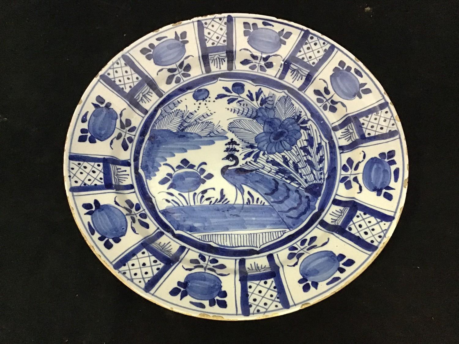 A large 18th Delft pottery charger painted with a peacock, fruit and flowers, 34.5cm wide