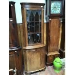 An oak corner cabinet, the cornice with dentil moulding above a bow-fronted glazed door enclosing