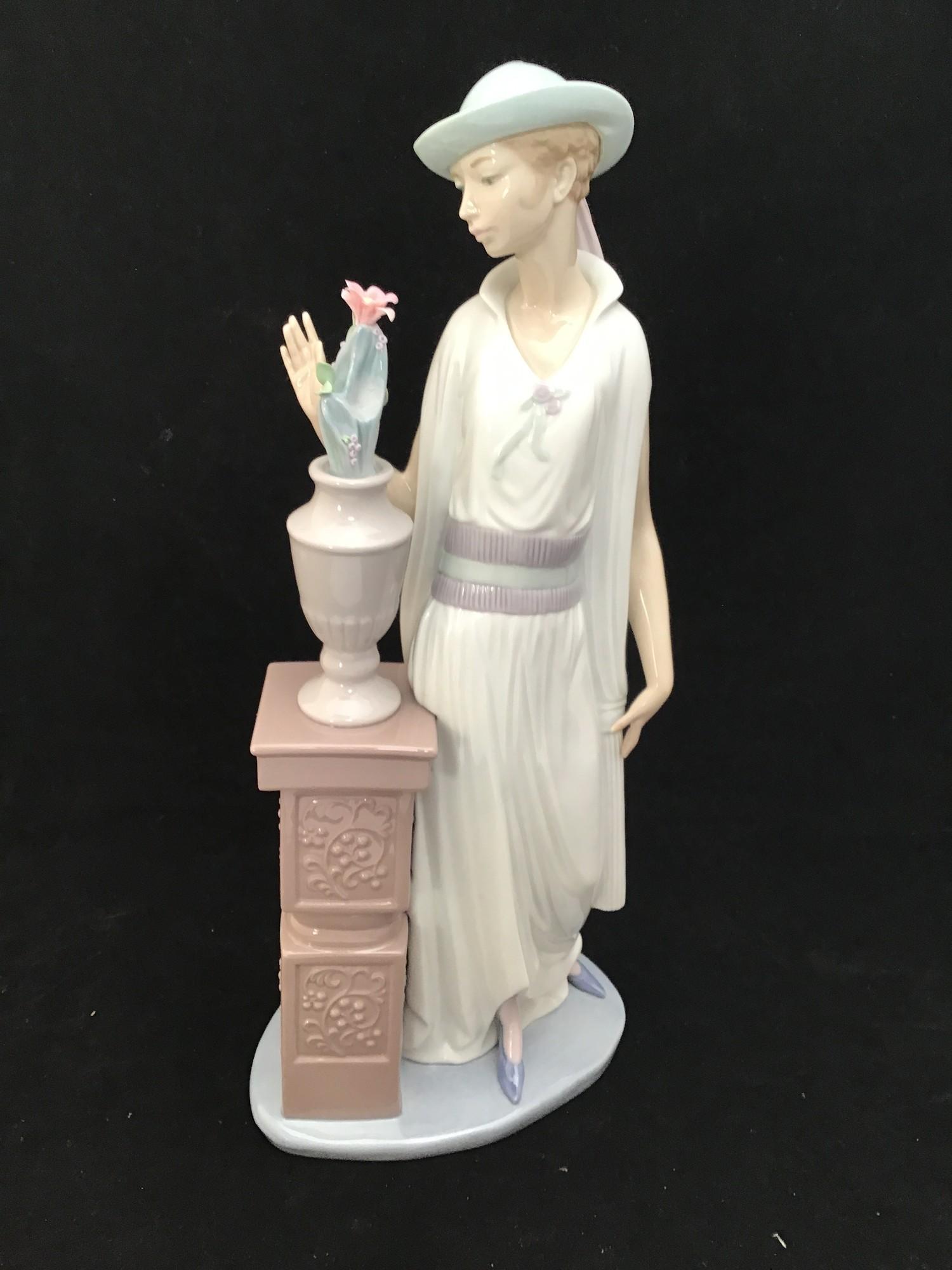 A large Lladro figurine of a lady in a long flowing dress and hat looking at a vase of flowers on