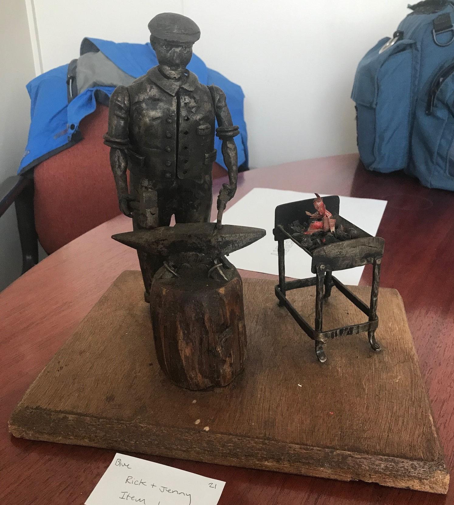 A modern patinated metal figure of a Blacksmith at his anvil and fire pit with hammer and tongs in