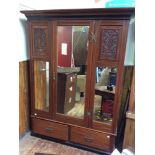 An Edwardian stained walnut wardrobe, with mirrored door flanked by mirror and floral vase carved