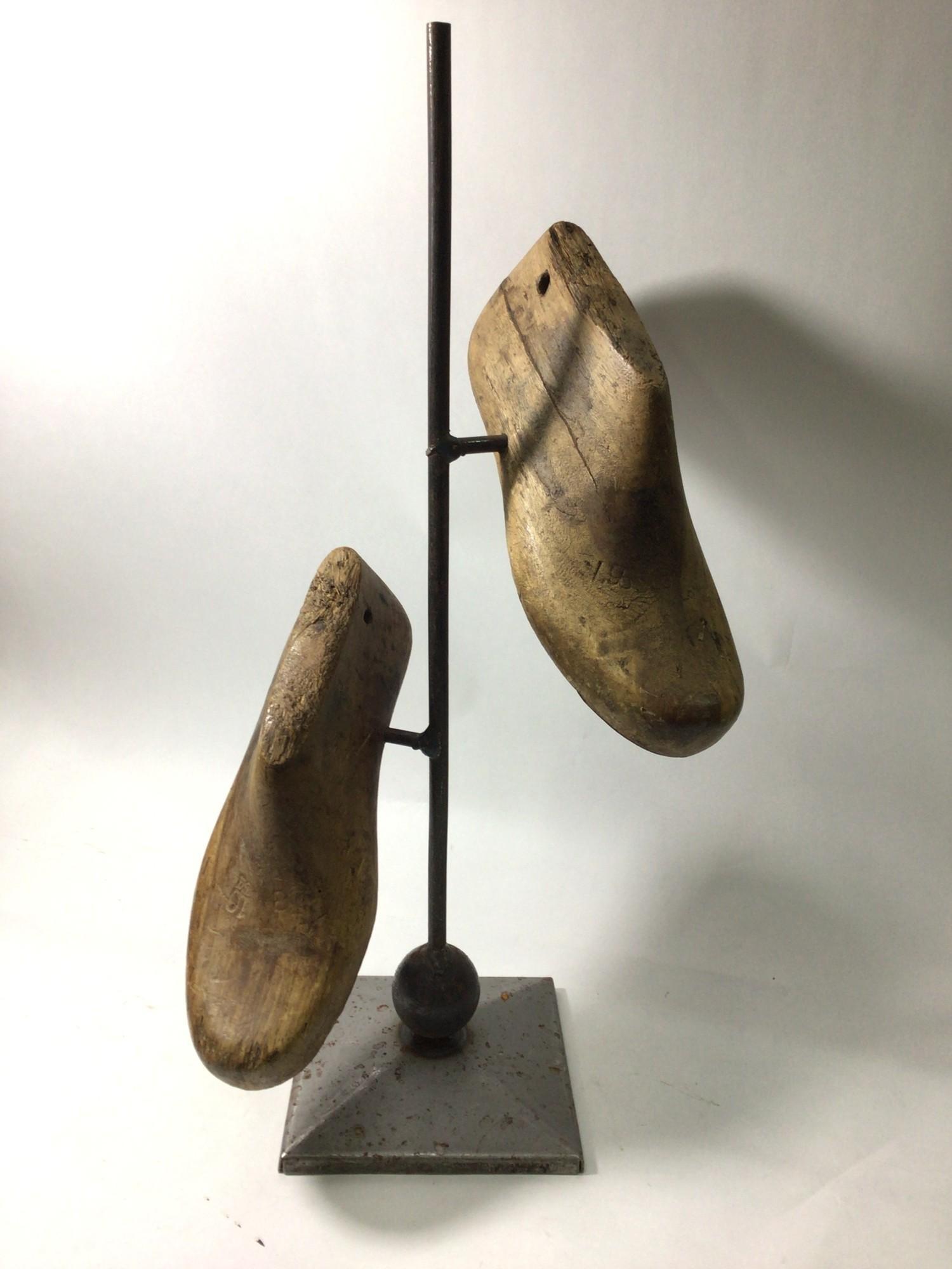 A modern sculpture of two antique cobbler's wooden shoe inserts suspended on a vertical metal