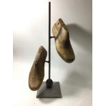 A modern sculpture of two antique cobbler's wooden shoe inserts suspended on a vertical metal