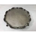 A George II silver salver with pie crust rim, raised on four scrolled feet, un-engraved central