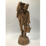 An early 20th century unglazed terracotta folk art figure of a man carrying baskets of grapes,