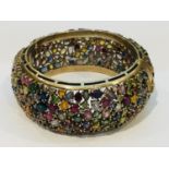 A 9ct yellow gold wide hinged bangle, encrusted with a variety of multi coloured gemstones including