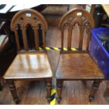 A pair of 19th Century oak hall chairs with gothic pierced tracery backs, raised on front