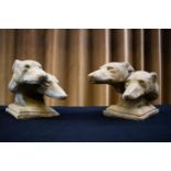 A pair of reconstituted stone sculptures, each modelled as two racing greyhound heads, raised on