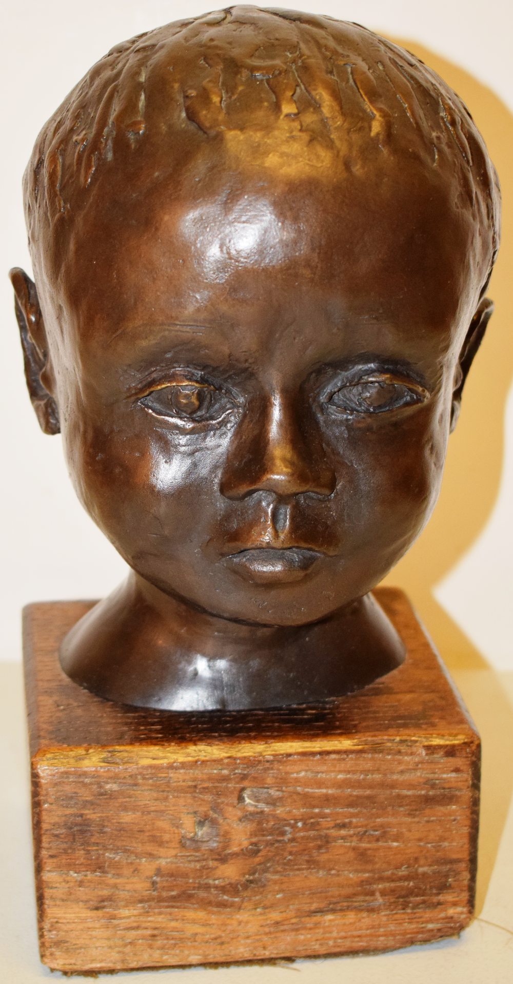 A bronze portrait bust of a child's head, the neck stamped with the