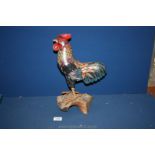 A hand carved and painted wooden cockerel with metal claws and standing on a gnarled wood base,