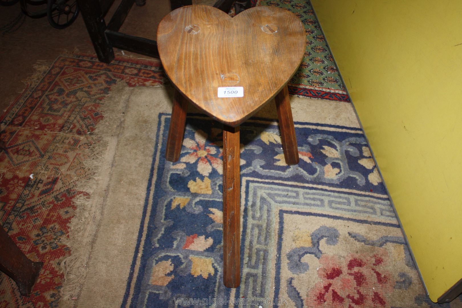 A primitive Arts and Crafts type stool having three splayed chamfered legs the top in the shape of