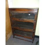 A three tier Oak finished set of up and over action glazed doored Bookshelves raised in turned legs