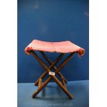 A bamboo folding stool having a red carpet seat.